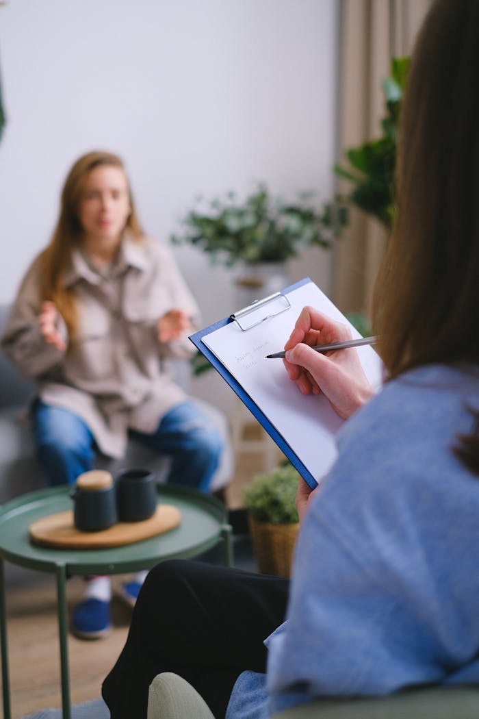 Home Unrecognizable female psychologist taking notes on clipboard while listening to patient sitting on blurred background during psychotherapy consultation in office